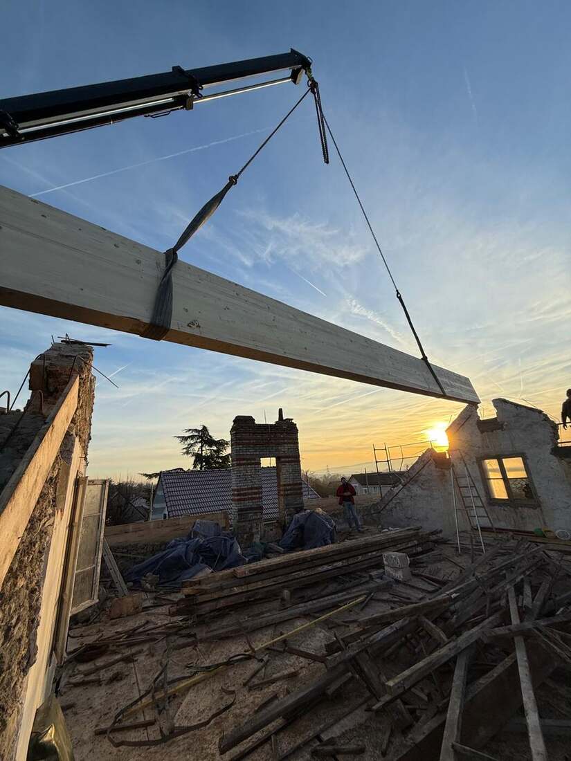Grue posant une poutre en bois sur un chantier au lever du soleil